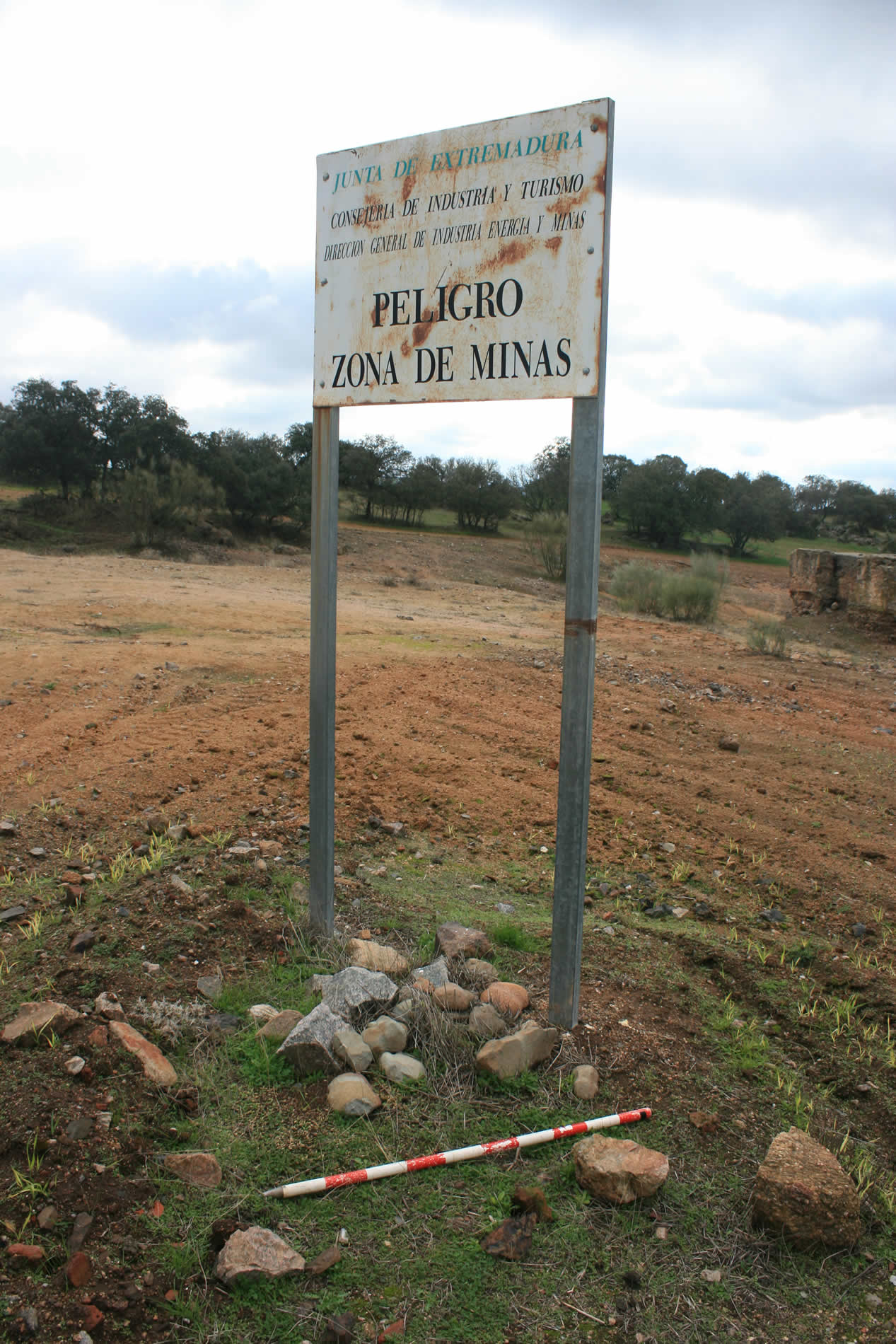  Peligro. Restauraciones medioambientales en áreas mineras 
  Concentración de mazas bajo el cartel de peligro en  Las Minillas-1, en una zona de la que se han retirado todos los escombros  mineros. El límite del enfoscado en la boca del pozo marca el nivel de  escombros original. La actividad minera, en sucesivas fases desde la  prehistoria en muchas de las mineralizaciones del sur de la Península Ibérica,  ha generado un patrimonio minero y metalúrgico excepcional. Ese patrimonio  formado durante milenios puede desaparecer en solo unos días debido a nuevos  proyectos de explotación minera o restauraciones medioambientales sin los  estudios arqueológicos previos especializados.